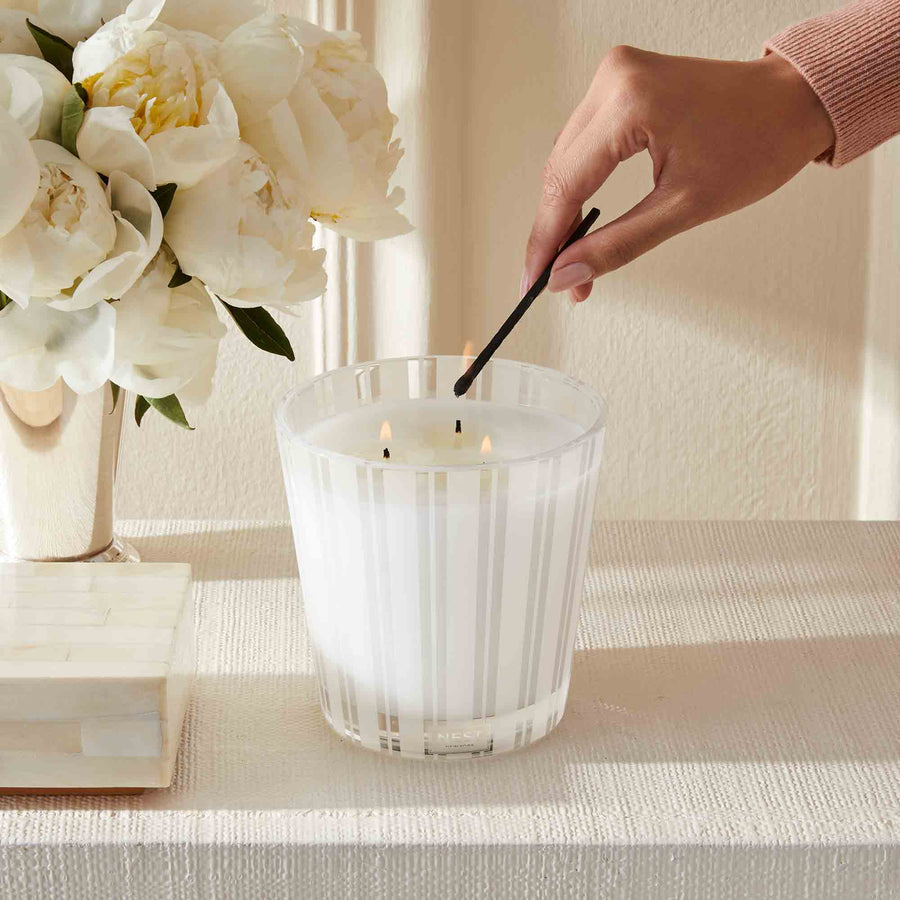 Velvet Pear 3-Wick Candle by NEST New York with hand, match, and flowers