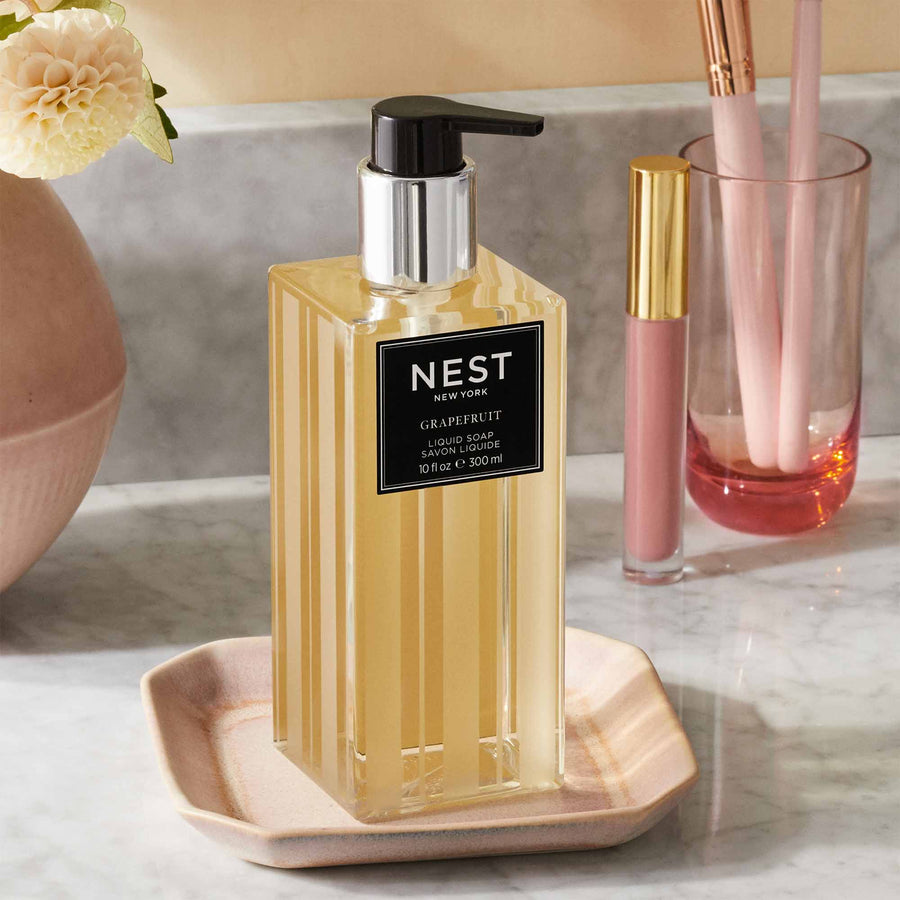 Grapefruit Liquid Soap by NEST New York with lip gloss, makeup brushes, and a flower